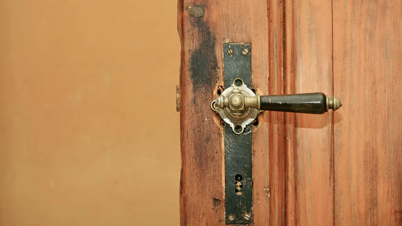 Une poignée de porte en laiton sur une porte de bois, contre un mur ocre